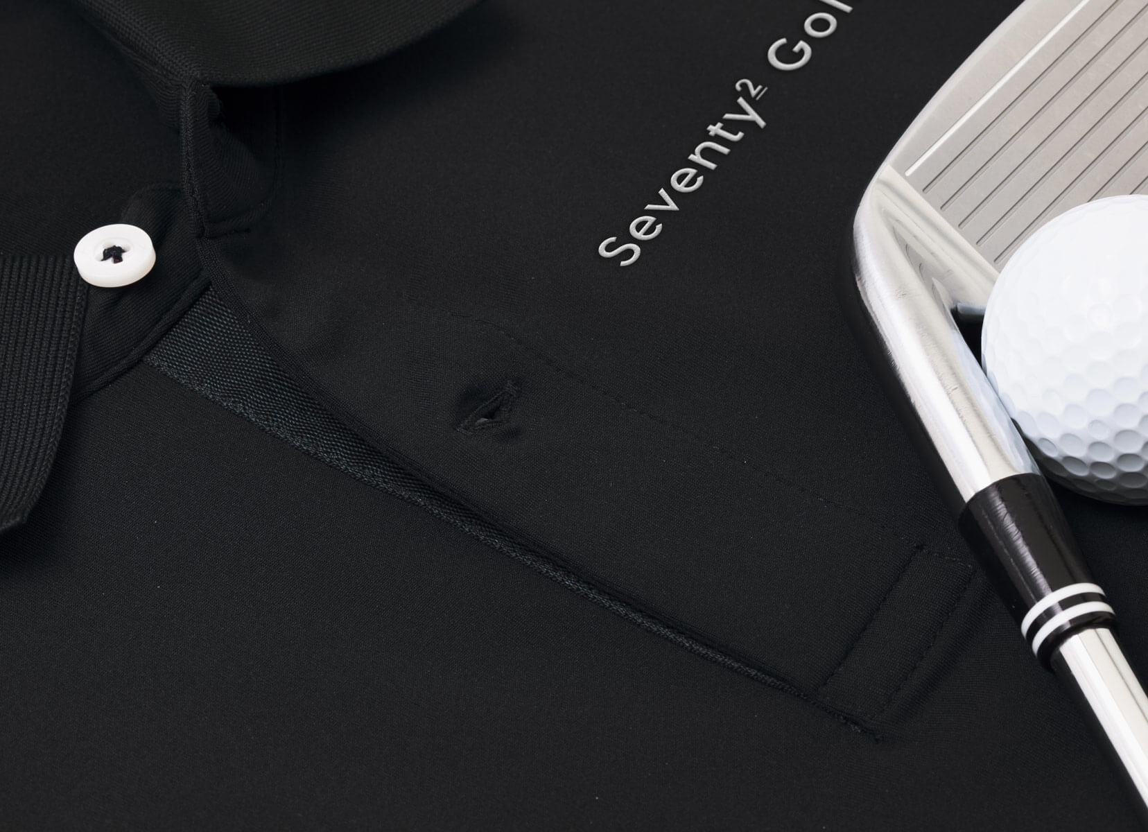Black polo shirt with white embroidered logo next to a golf club and ball
