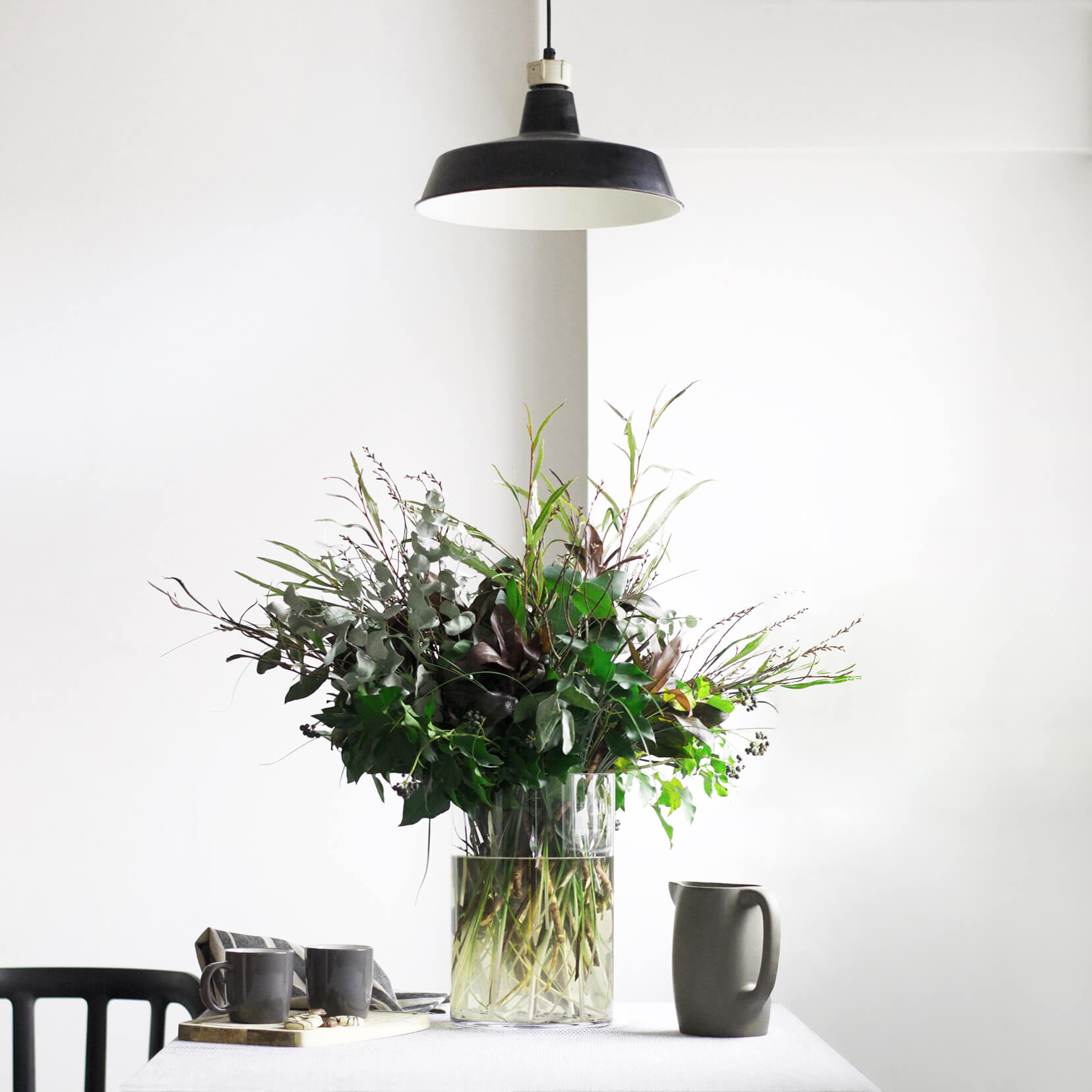 Bunch of greenery arranged in a vase on dining table with tea being served