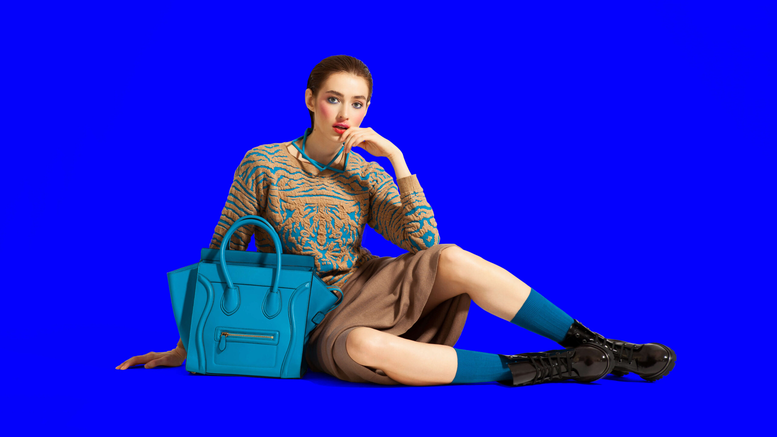 Fashion model sitting next to bag on bright blue background